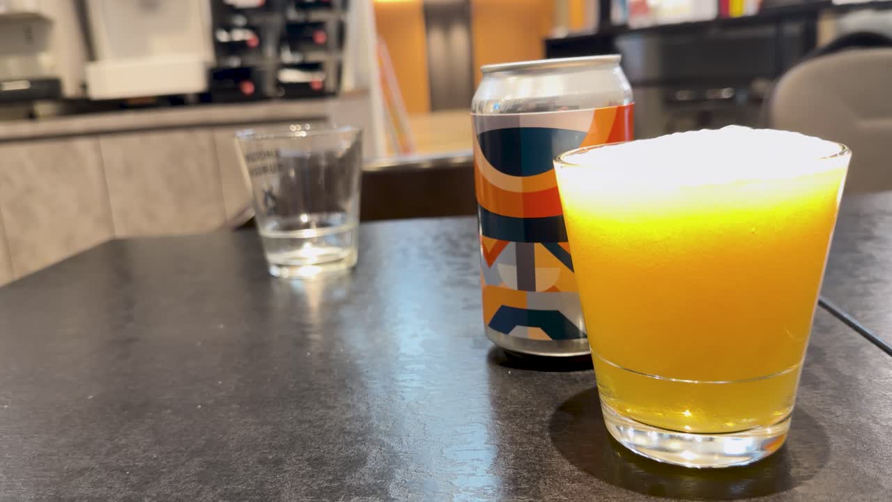 Bir restoran ortamında cam bir bardağa dökülen altın renkli lager bira, kalın beyaz köpük oluşturuyor.