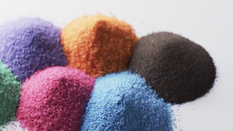 Video-of-close-up-of-heaps-of-multi-coloured-sand-grains-and-copy-space-on-white-background