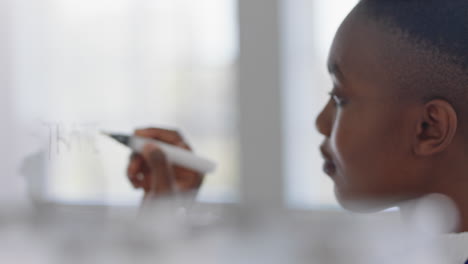 Mujer-De-Negocios-Afroamericana-Escribiendo-En-Una-Pizarra-De-Vidrio-Intercambiando-Ideas-Para-La-Estrategia-De-Resolución-De-Problemas-En-La-Oficina