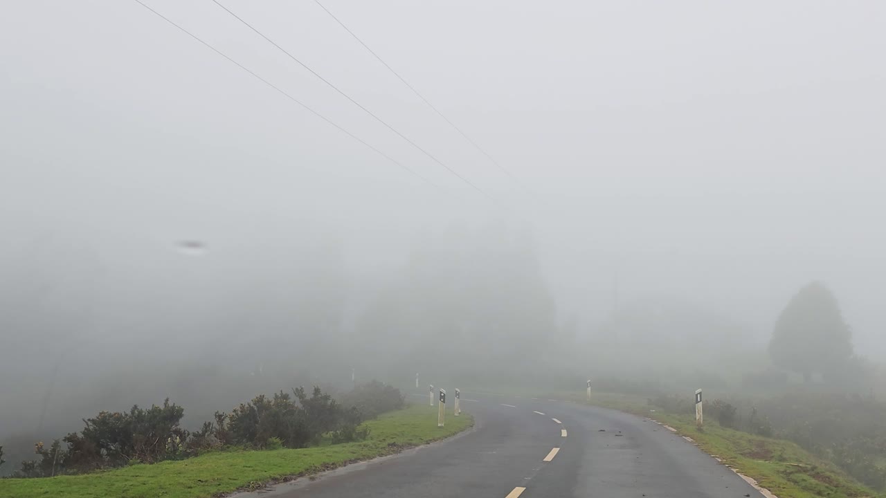 Névoa densa cobrindo estrada de montanha durante tempo tempestuoso na Madeira com baixa visibilidade, vento forte, atmosfera sombria e condições dramáticas criando imagens de viagem cinematográficas e tensas