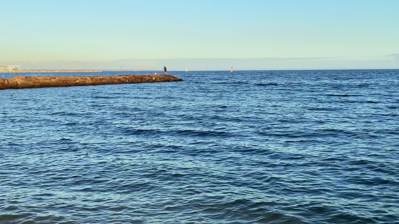 한 남자가 석양 바다에서 암벽 낚시에 서 있다