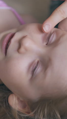 careful mother cures cute little girl eyes with clear medical drops on soft beige bed in light room close upper view