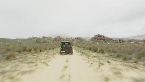 drone flies fast over the ground behind a black off-road vehicle over desert landscape and through rock formations in the cederberg wilderness area in south africa - drone tracks the car