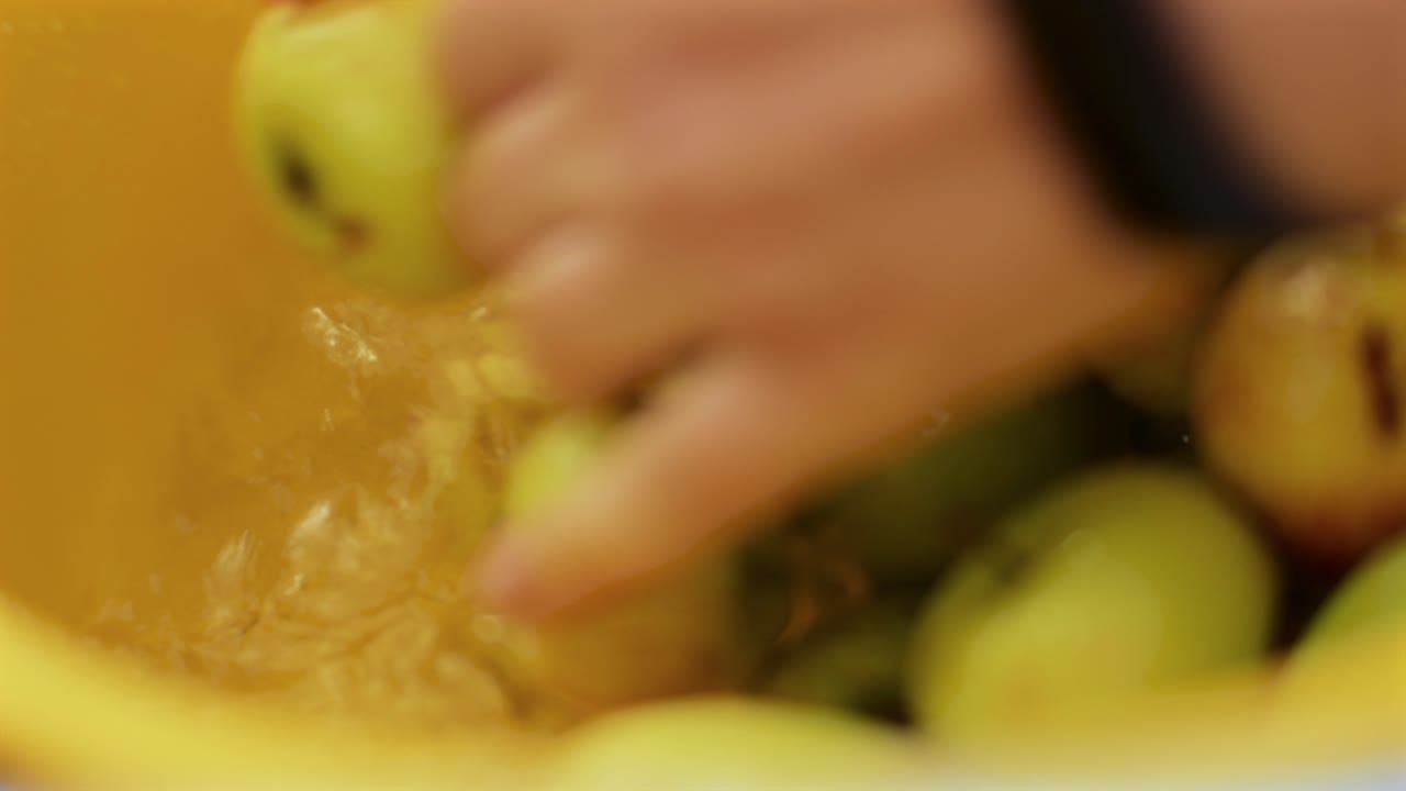 cerca de las manos de la mujer lavando manzanas verdes en un cubo amarillo