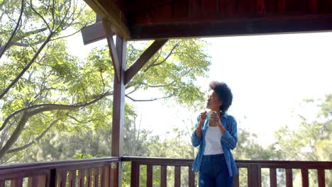 Fröhliche-Afroamerikanische-Frau-Trinkt-Tee-Auf-Der-Sonnigen-Terrasse,-In-Zeitlupe