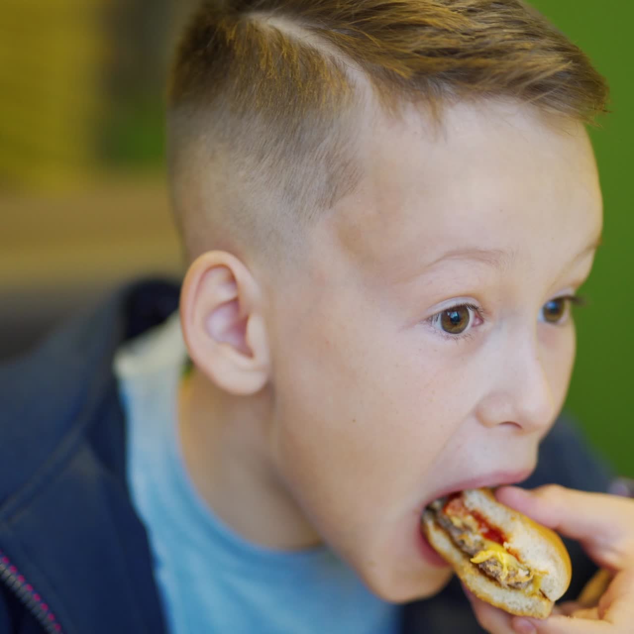Young happy teenager eating fries and burger sitting in cafe in city. Boy in a fast food cafe. Harmful nutrition