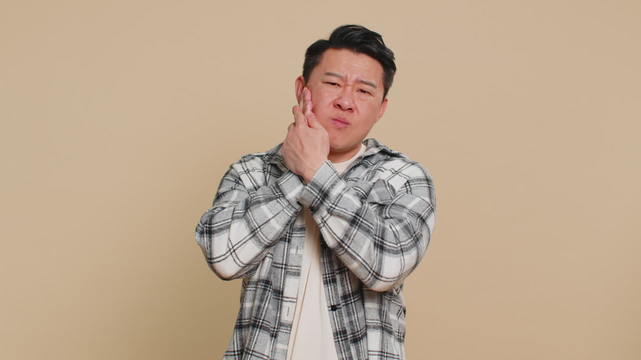 Asian man touching cheek closing eyes with expression of terrible suffer from painful toothache