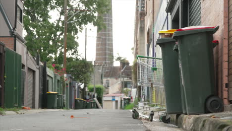 Un-Carrito-De-Compras-Robado-Se-Encuentra-Detrás-De-Dos-Contenedores-Con-Ruedas-En-Una-Tranquila-Calle-Urbana-En-El-Interior-Del-Oeste-De-Sydney,-Australia