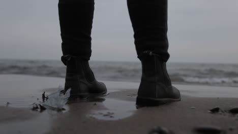 a person wearing a black leather boots standing in the shoreline - close up shot