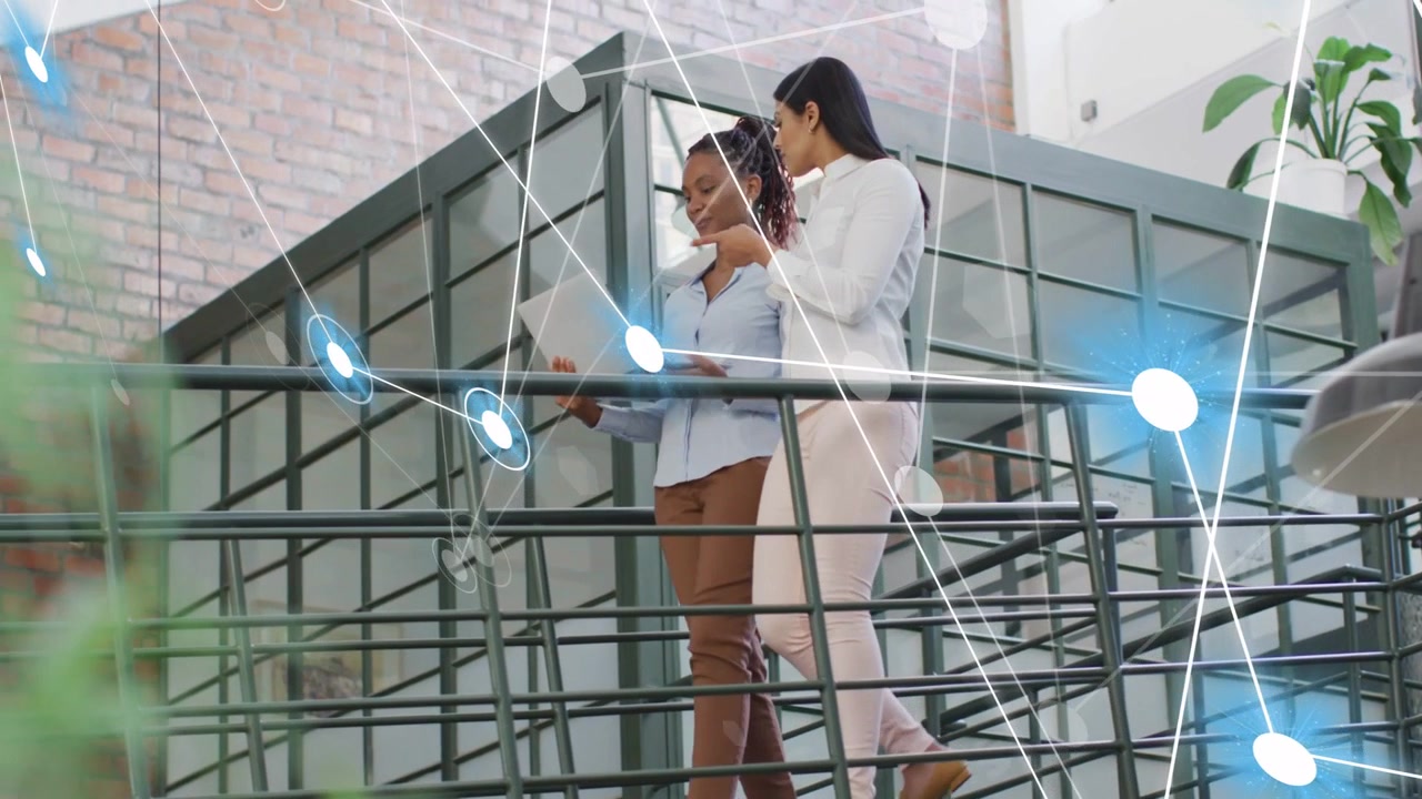 Two coworkers walking mezzanine, left one opening laptop causing blue nodes showing business data