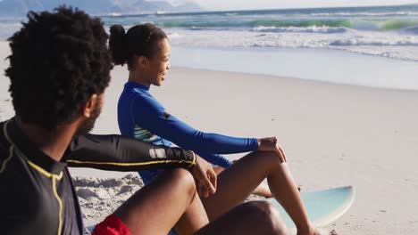 pareja afroamericana hablando y sentada de tablas de surf en la playa