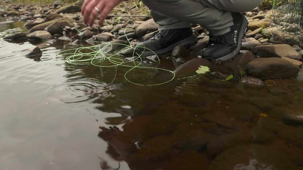 fotografía de mano de un pescador de mosca liberando una pequeña trucha marrón de nuevo en el río