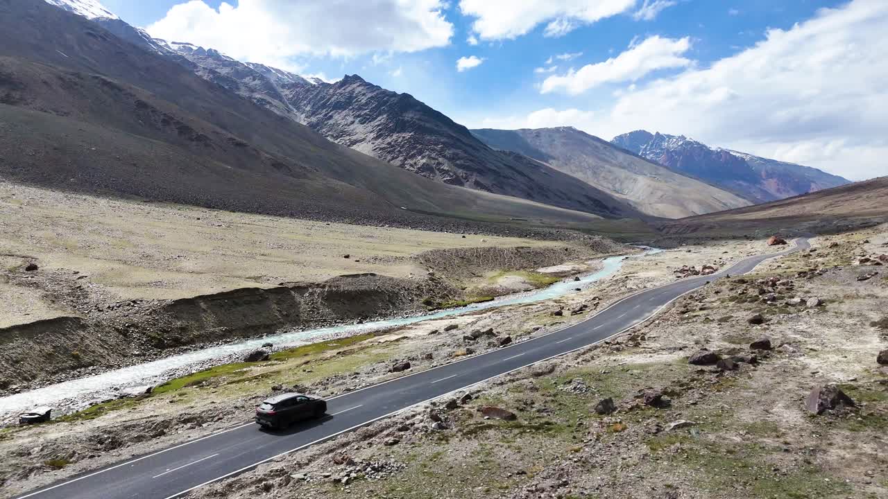 Aerial drone shot capturing a car driving steadily along a straight mountain road in Ladakh.