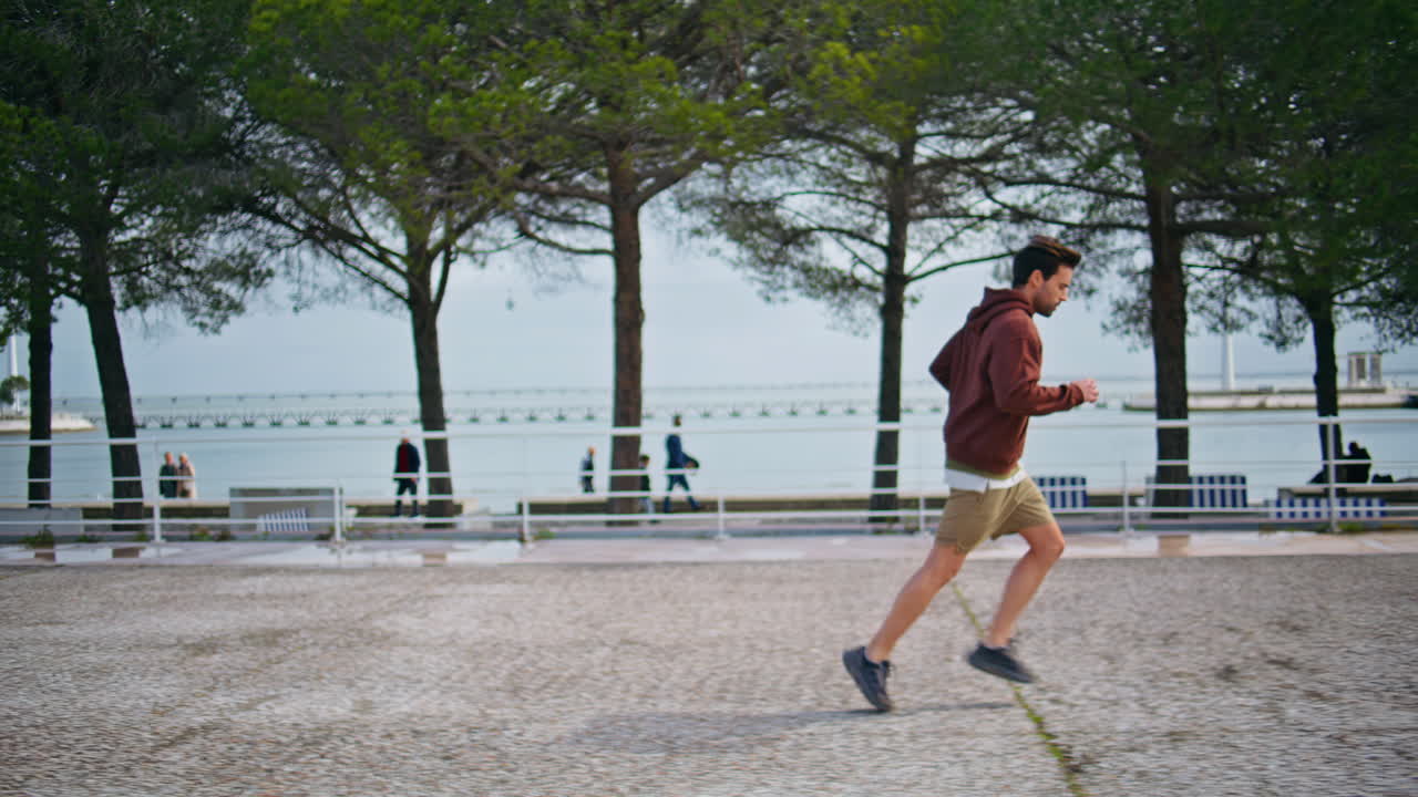 Runner training urban riverside in cloudy morning. Brunette athlete sprinting