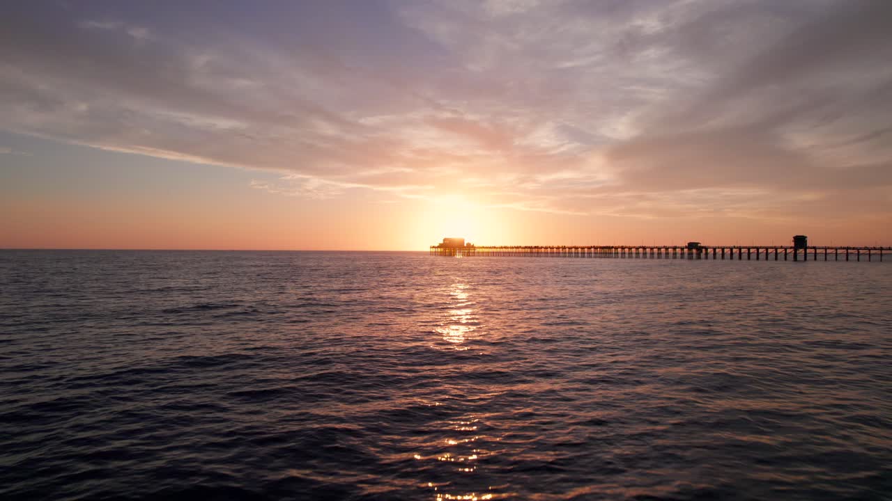 황금시간대 일몰에 바다 쪽 부두를 가로질러 물을 가로질러 날아가는 드론