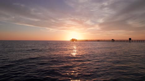 Drone-Volando-A-Través-Del-Agua-Sobre-El-Muelle-De-Oceanside-En-La-Puesta-De-Sol-De-La-Hora-Dorada