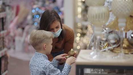 una madre con una máscara médica con su hijo en el centro comercial elige decoraciones para la casa para navidad. víspera de navidad durante la pandemia
