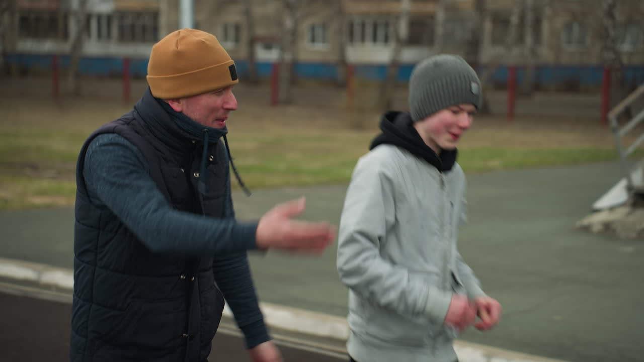 Close-up of a coach jogging alongside a young boy in a stadium, the coach is engaged in conversation with the boy, who is smiling