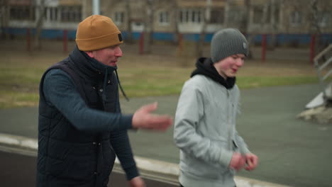 Close-up of a coach jogging alongside a young boy in a stadium, the coach is engaged in conversation with the boy, who is smiling