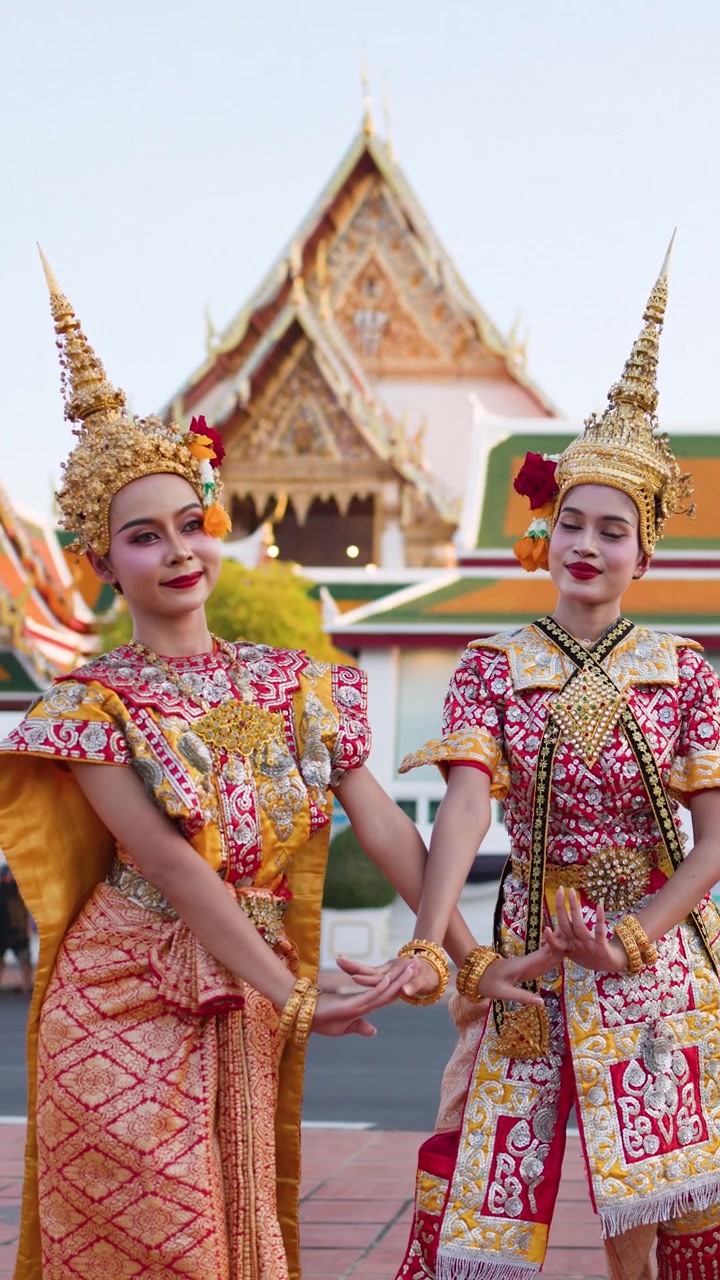 Dos mujeres con elaborados trajes dorados realizan movimientos de danza tradicional tailandesa fuera de un templo de Bangkok