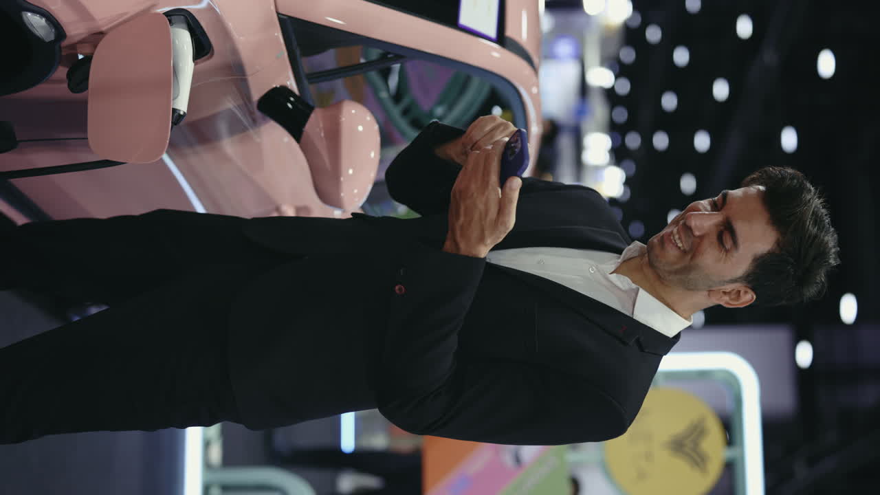 Businessman looking at smartphone near pink electric car at an exhibition