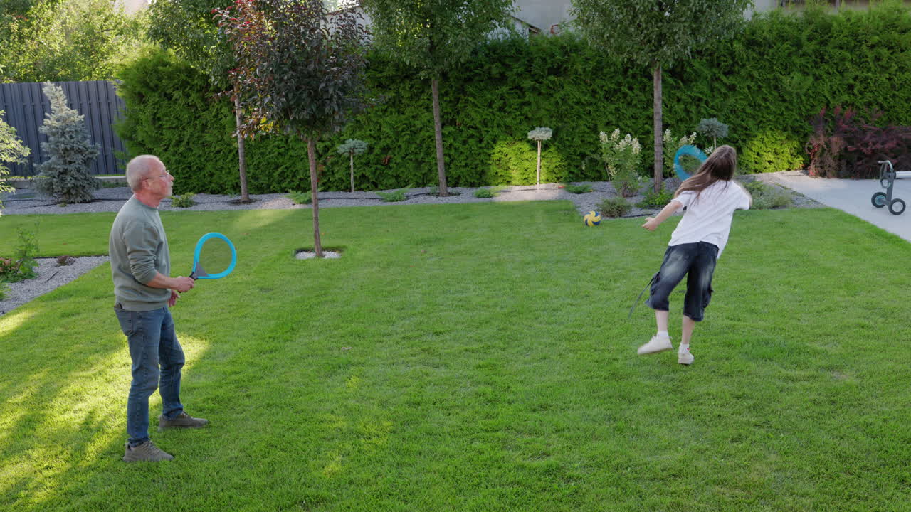 Active Grandfather Playing Racket Game With Granddaughter In Backyard Garden