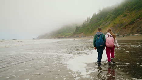 two children walking along a foggy beach with cliffs in the background