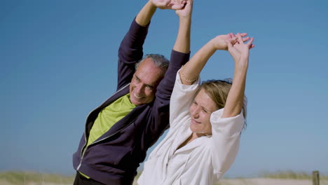 happy senior couple raising arms up and bending to sides outdoor