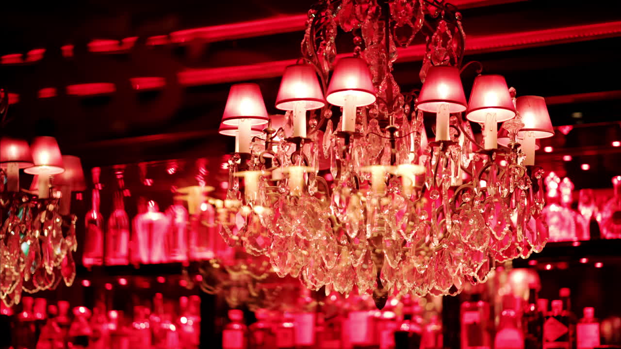 Chandeliers with red lighting on the ceiling at a restaurant with shelves of alcohol on the back