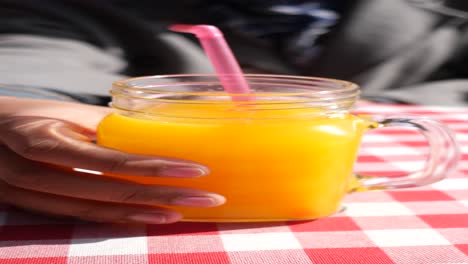 una mano sosteniendo un vaso de jugo de naranja con una pajita rosa