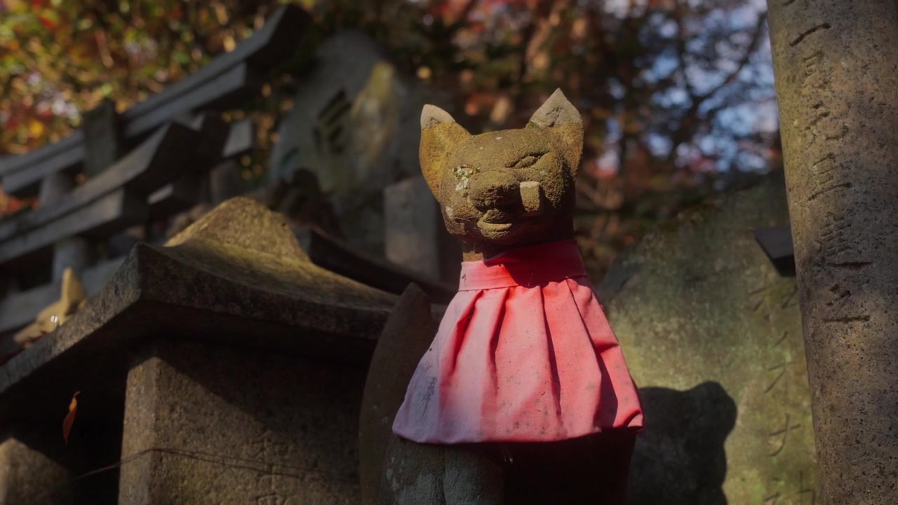 Primo piano di una statua di volpe Inari in un santuario giapponese con bavaglino rosso. Calda luce autunnale e atmosfera tradizionale