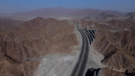 4k: rear drone view of uae mountain range, traffic movement in between the khorfakkan mountains, sharjah, united arab emirates