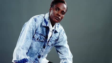 androgynous man in denim jacket posing against grey background