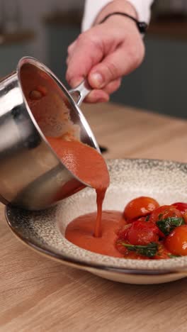chef pouring tomato soup into a bowl with cherry tomatoes