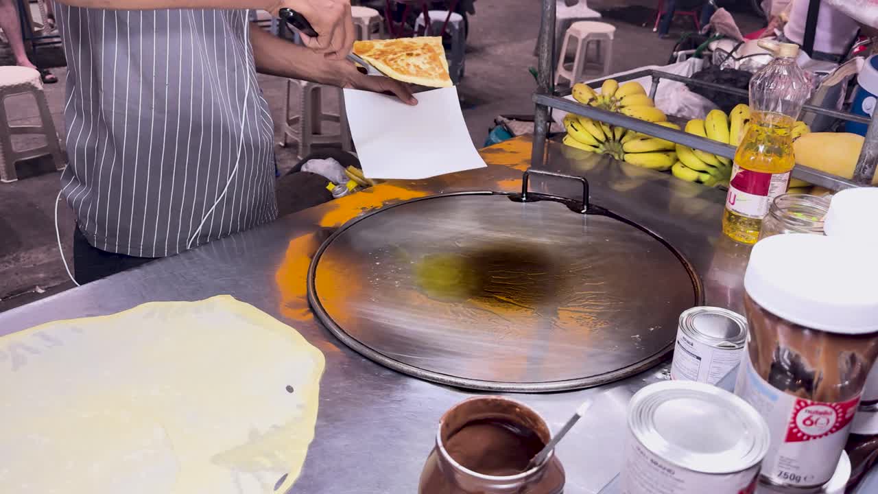 un vendedor callejero en phuket prepara roti tailandés en una parrilla caliente, mostrando técnicas tradicionales de comida callejera en una iluminación vibrante