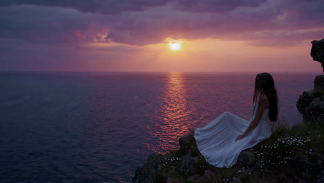 woman watching sunset from cliff overlooking the ocean