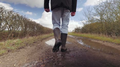 3-4 shot of man walking in puddles in the countryside with wellington boots on