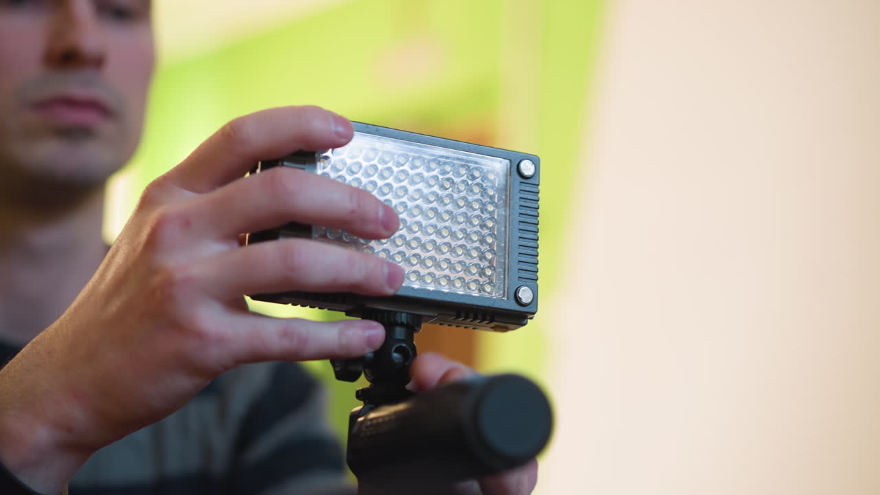 Studio guy adjusting camera equipment, holding gear above microphone on tripod. Focus on hand and camera setup, blurred background with soft lighting. Indoor video production setup