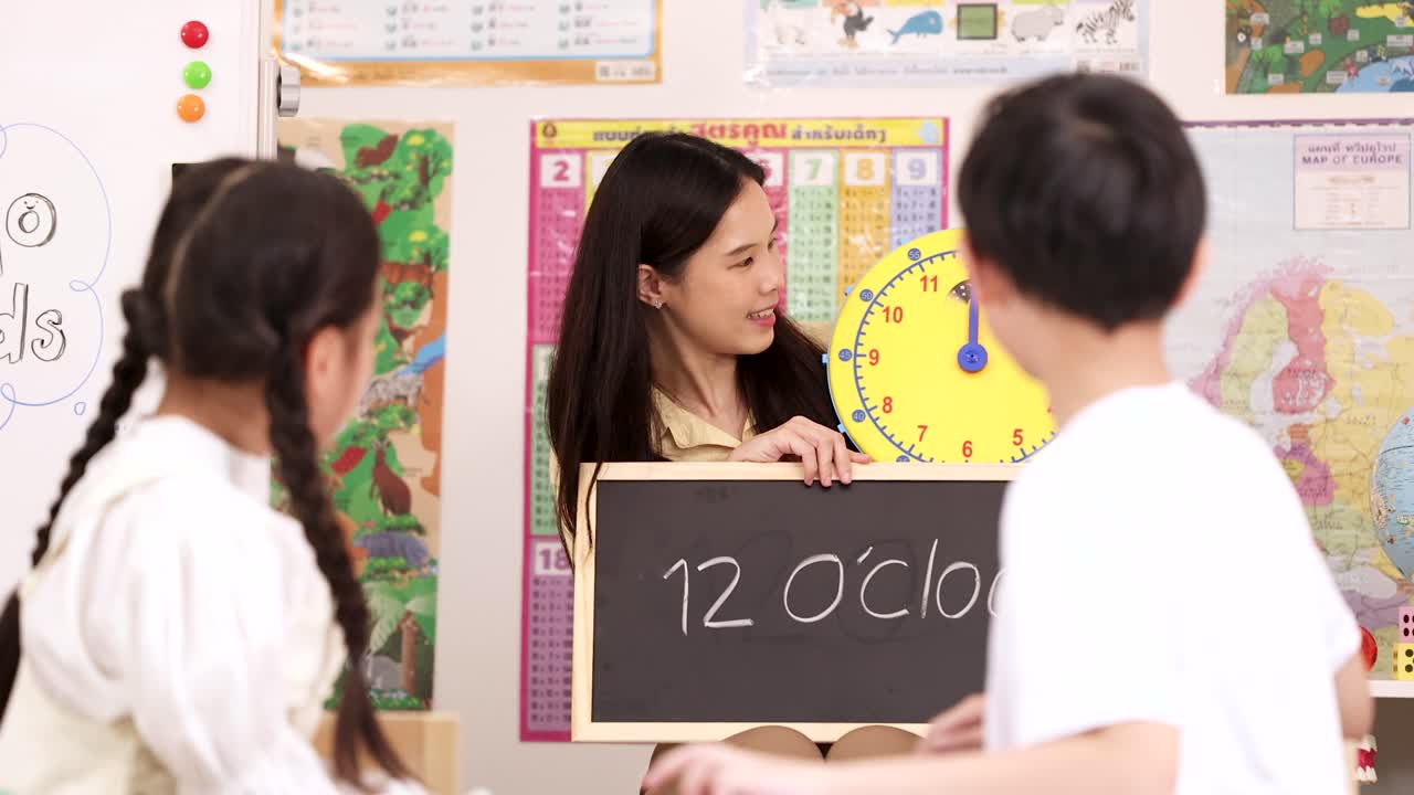 笑顔の小学校教師が、2人の子供たちに教室の時計で12時を読むように教えています。