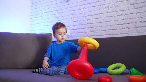 little kid playing with pyramid on the sofa. happy active toddler disassembling the toy and rejoicing.