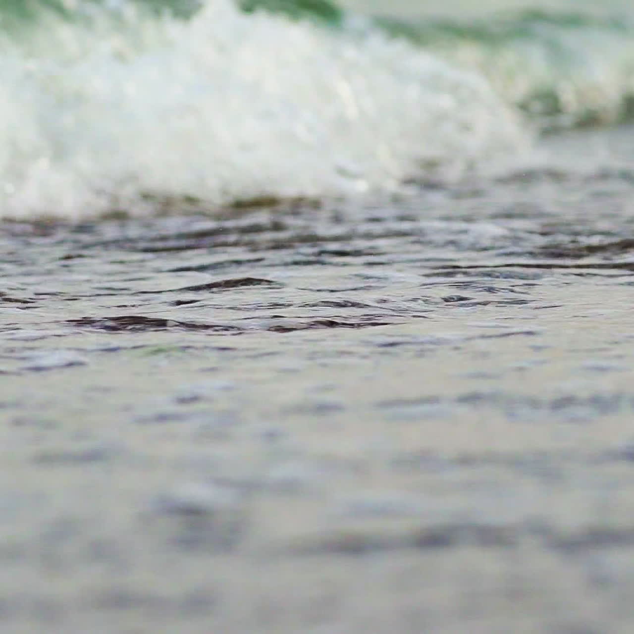 Flowing sea water on the beach with white foam in the evening. The edge of the ocean with foam waves hitting into the shoreline background. Close-up.