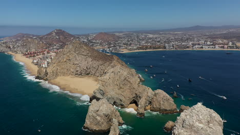 drone shot of resorts on playa el médano then revealing playa del amor, lover's beach, and el arco, a natural archway in the sea cliffs in cabo san lucas mexico, wide and rotating