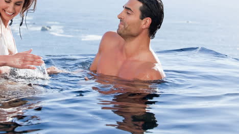 una pareja caucásica sonriente de vacaciones salpicándose en el mar.