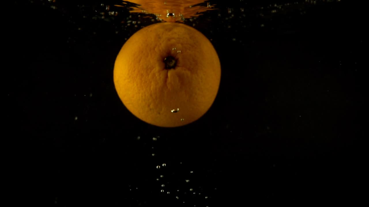 Caduta di arancia nell'acqua. Movimento rallentato. Sfondo nero.