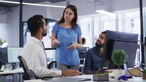 caucasian businesswoman standing in discussion with two mixed race male colleagues at their desk