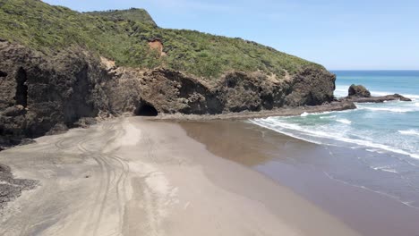 playa pintoresca con turistas caminando por la orilla arenosa en la playa de bethells, auckland, isla del norte, nueva zelanda - descenso aéreo