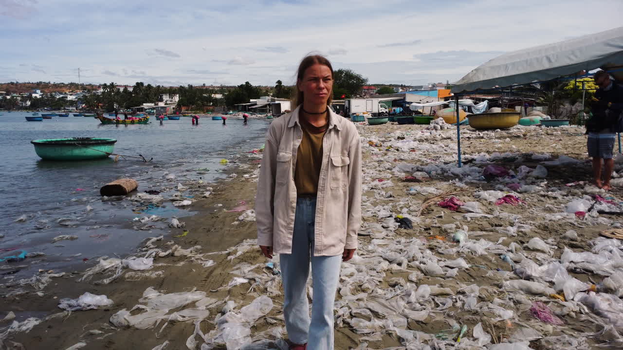 Giovane donna caucasica che indossa abiti ecologici e sostenibili, che cammina con sandali a piedi nudi su una spiaggia tropicale con inquinamento da rifiuti di plastica.