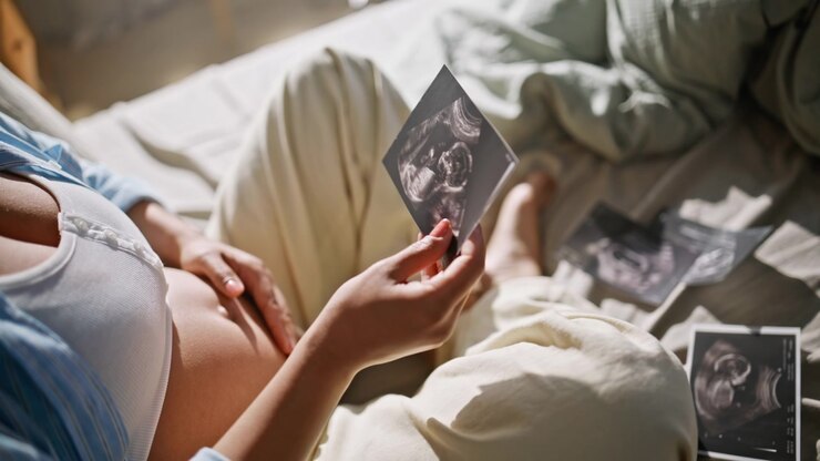 Foto ecografiche, mani di donna incinta in primo piano. Madre in attesa su lettino ecografico