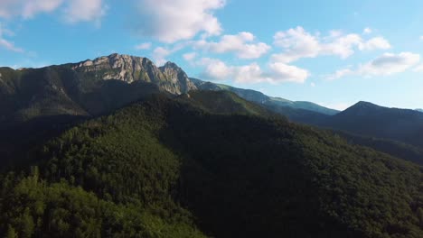 Aerial-Shot-in-Alpine-Village-Epic-Mountain-Peaks,-Hills-Covered-With-Pine-Trees-in-Haze,-Sunrise-Light