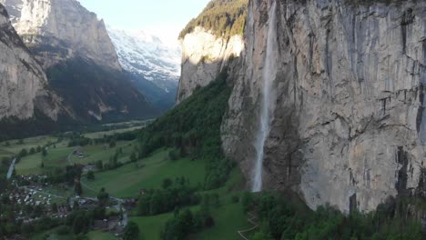 Vista-Aérea-De-Una-Cascada-Alta-En-Un-Valle-Cerca-De-Un-Pequeño-Pueblo